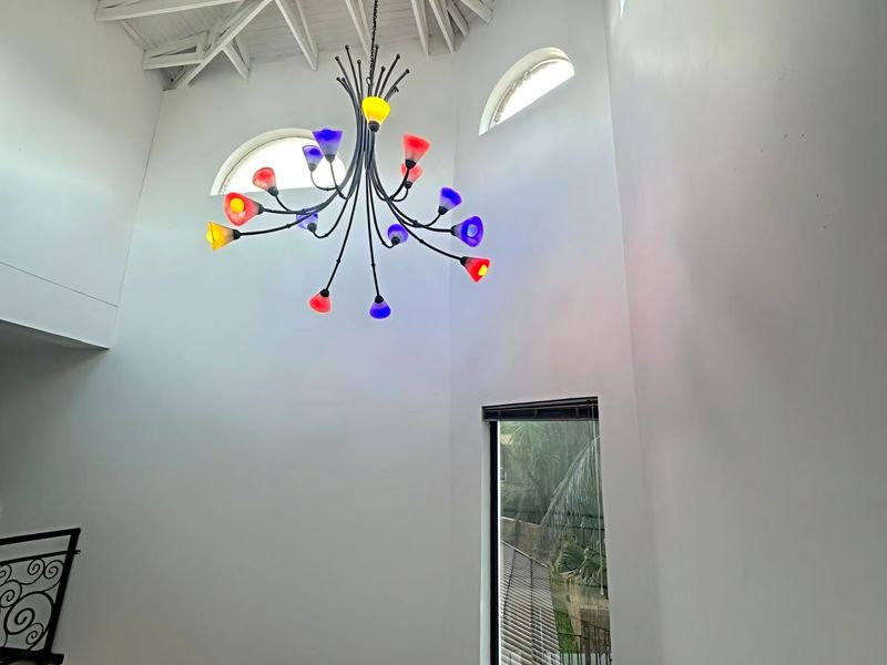 A bright, double-volume entrance hallway featuring a vaulted ceiling with exposed trusses, arched windows, and a decorative multi-colored chandelier.