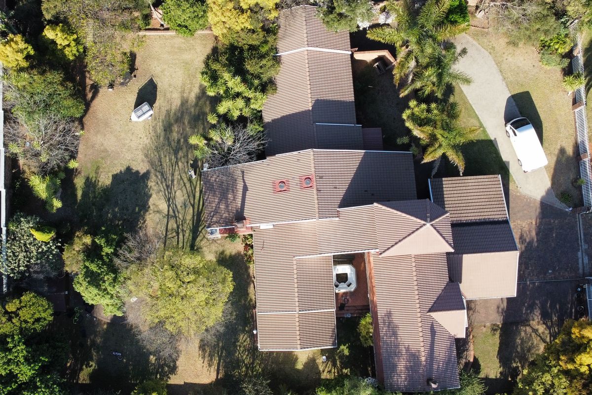 Aerial view of the property showcasing the expansive roof structure, paved driveway, and established garden surroundings.