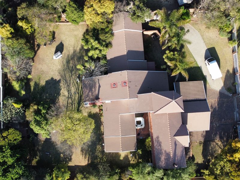 Aerial view of the property showcasing the expansive roof structure, paved driveway, and established garden surroundings.