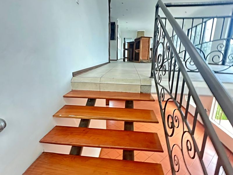 A staircase with wooden treads and a decorative wrought iron balustrade leading to an upper level with tiled flooring.