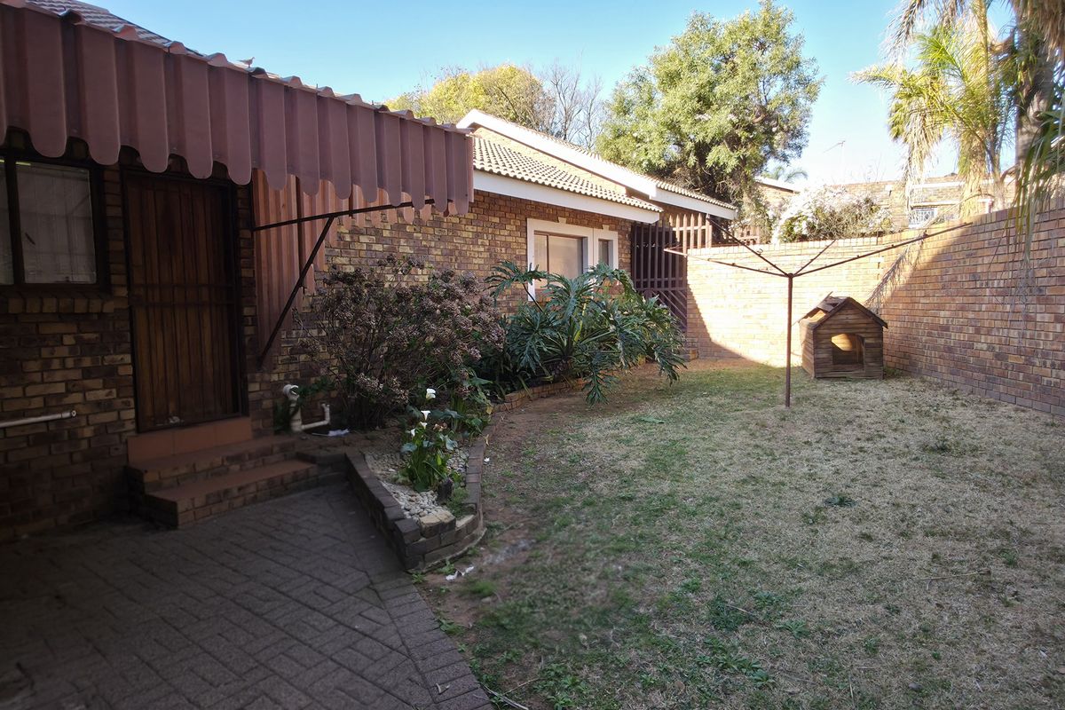 A private rear garden featuring a paved patio area, brick boundary walls, and a metal awning over the entrance.