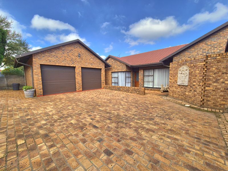 Front view of a face brick house featuring a double garage with roller shutter doors and a spacious paved driveway.