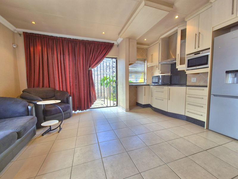 Open-plan kitchen and living area featuring tiled flooring, built-in cabinetry, integrated appliances, and direct access to an outdoor space via a sliding door.