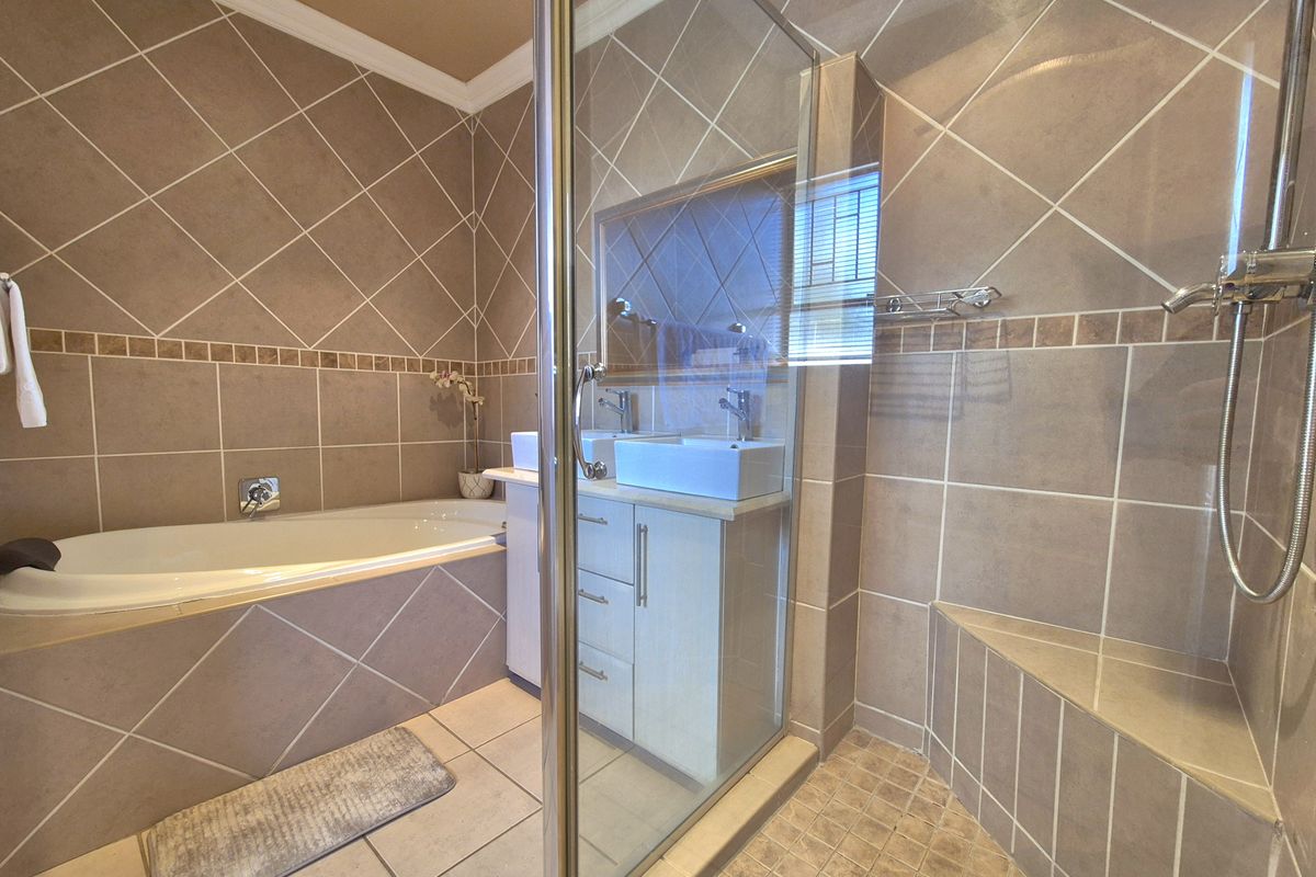 A well-maintained bathroom featuring a built-in bathtub, a glass-enclosed shower with a built-in bench, and a double vanity with modern basins.