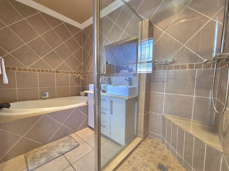 A well-maintained bathroom featuring a built-in bathtub, a glass-enclosed shower with a built-in bench, and a double vanity with modern basins.