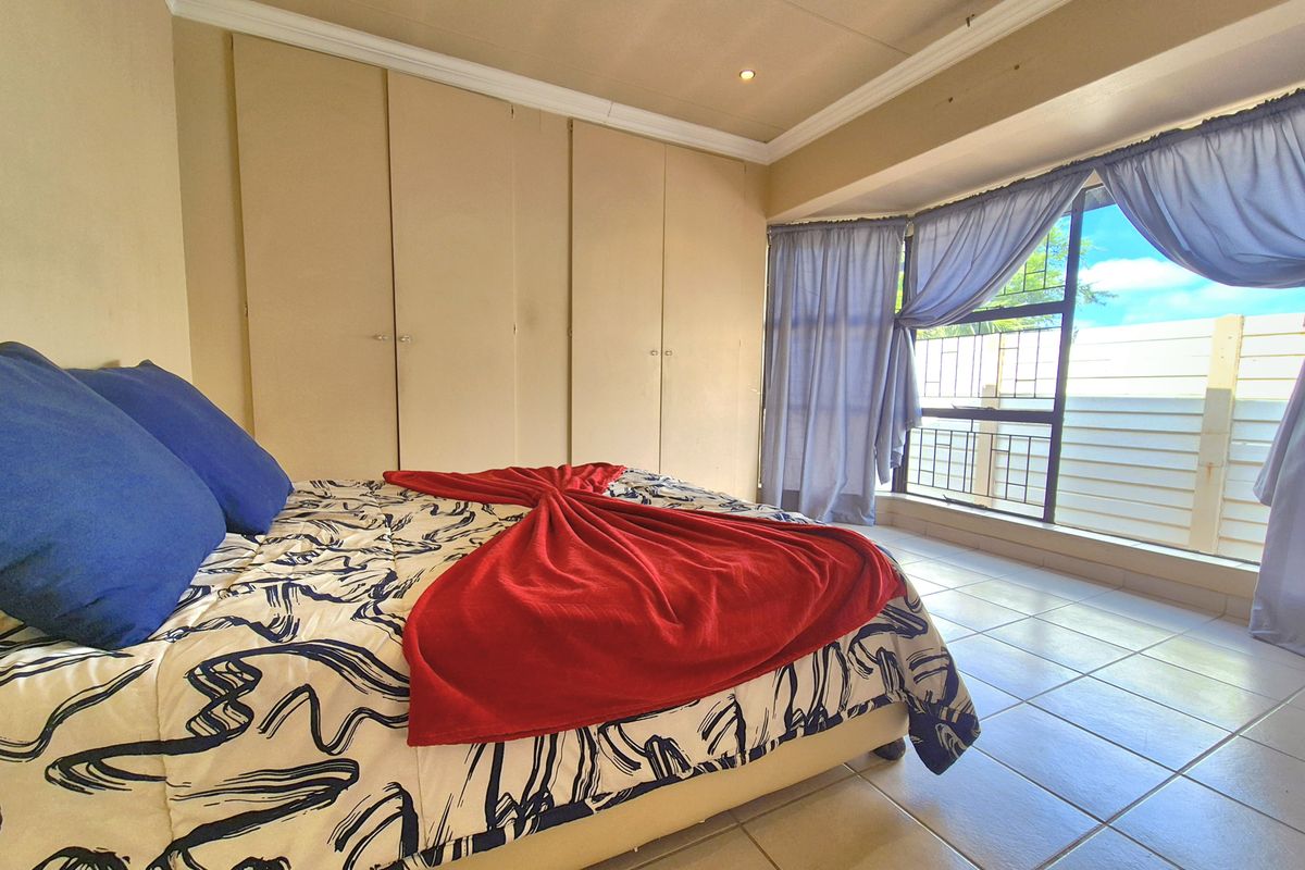 A bedroom featuring built-in cupboards, tiled flooring, and large windows with security bars, offering a functional space with potential for cosmetic updates.