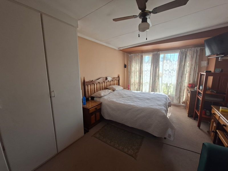 A bedroom featuring built-in cupboards, a ceiling fan, and large windows with natural light. The room requires cosmetic updates to modernize the finishes.