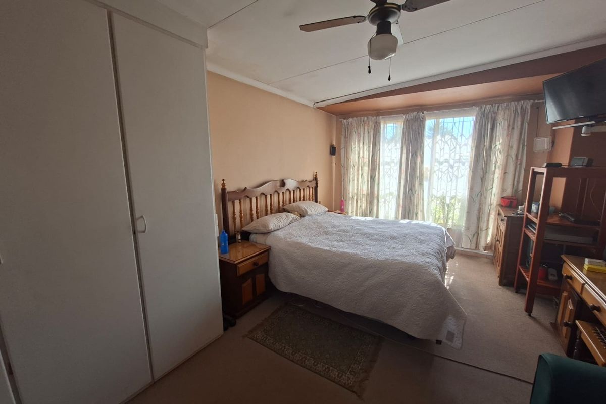 A bedroom featuring built-in cupboards, a ceiling fan, and large windows with natural light. The room requires cosmetic updates to modernize the finishes.