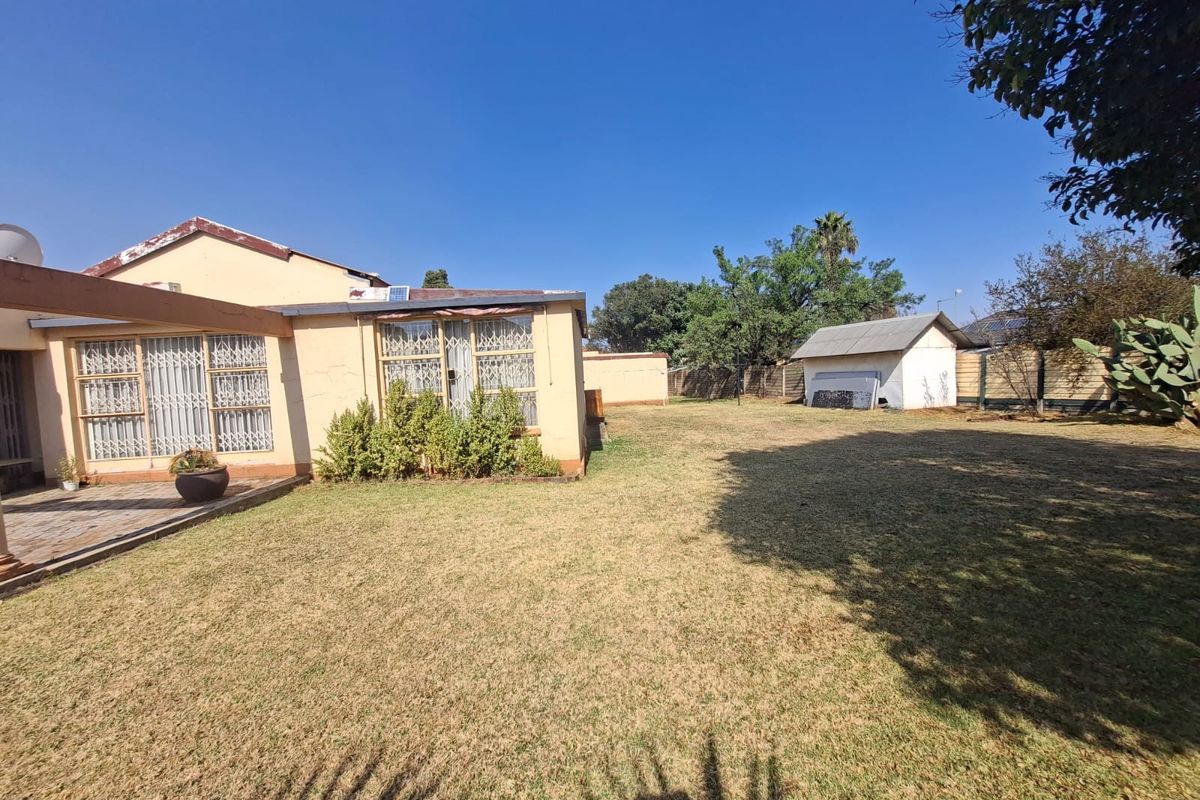 Rear view of the property featuring a paved patio area, a large lawn, and a detached outbuilding within a fenced garden.