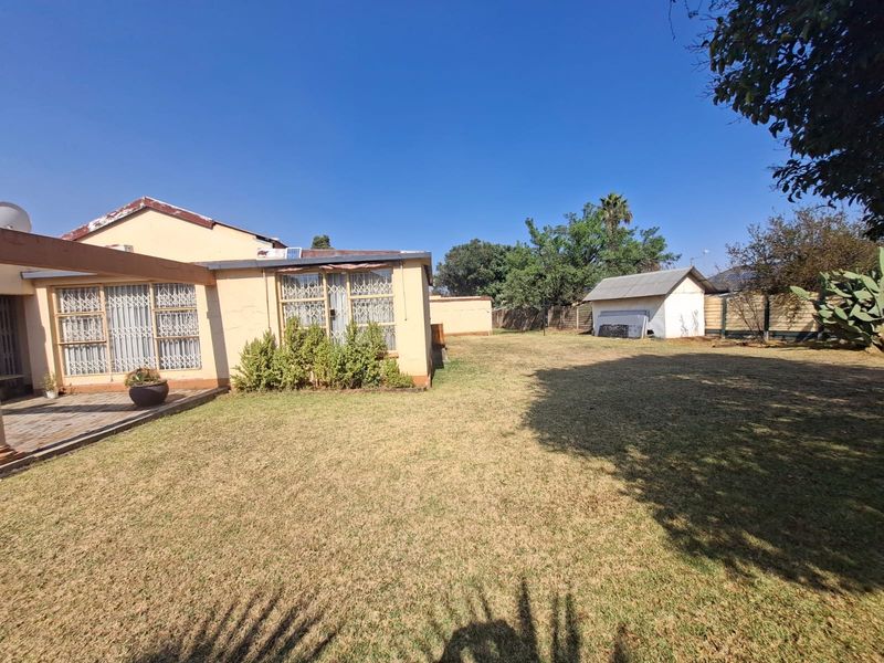Rear view of the property featuring a paved patio area, a large lawn, and a detached outbuilding within a fenced garden.