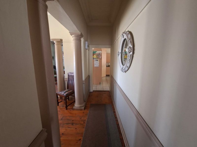 A classic hallway featuring timber flooring, decorative columns, and wainscoting, leading through an archway towards the kitchen area.