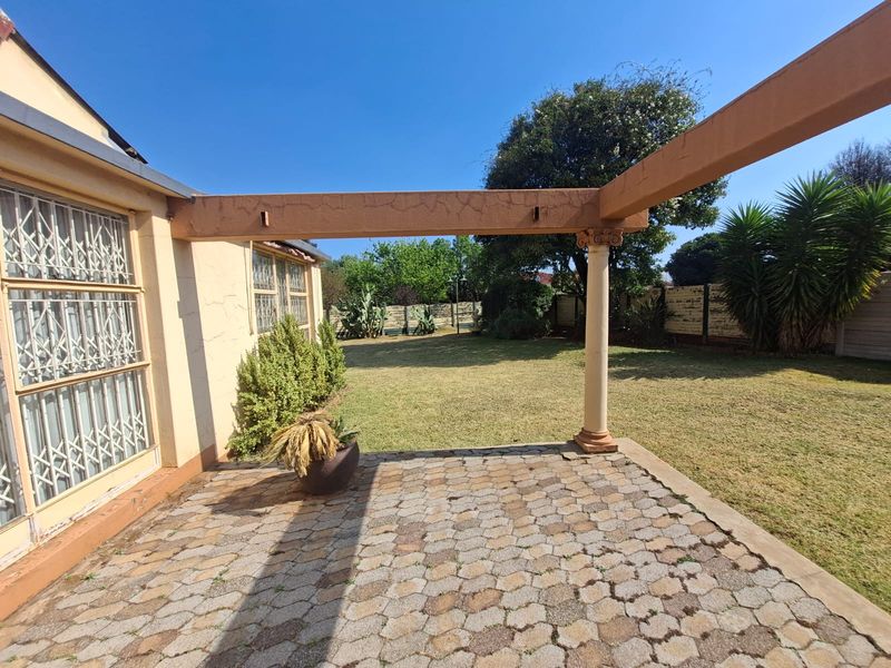 Outdoor paved patio area featuring a pergola structure with a classical column, overlooking a private garden space.