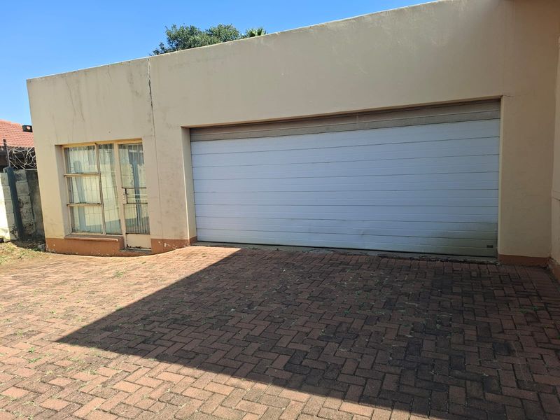 Exterior view of a single garage featuring a sectional door, paved driveway, and adjacent window with security gate.