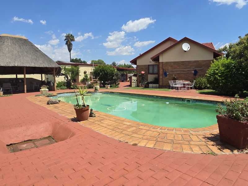 Outdoor pool area featuring a swimming pool, a traditional thatched lapa, and extensive brick paving, set within a private garden space.