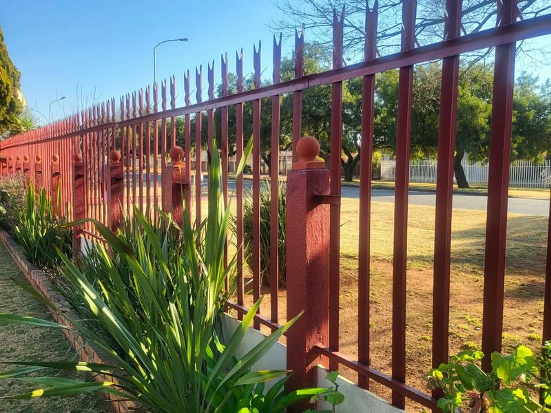 A view of the property's street-facing metal palisade security fencing with a brick masonry base and established garden border.