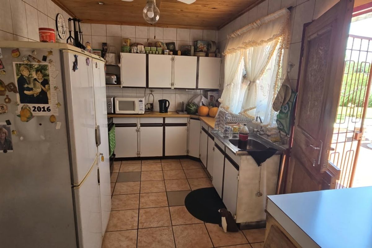 A dated kitchen featuring tiled flooring, timber ceiling, and built-in cabinetry with a direct access door to the exterior.