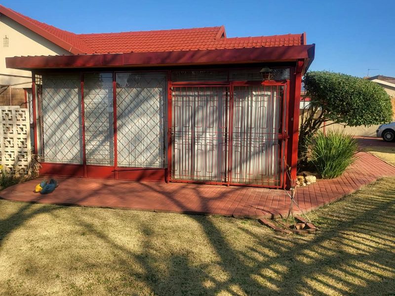 Enclosed patio area featuring red metal security gates and window frames, set on a paved terrace with a tiled roof.