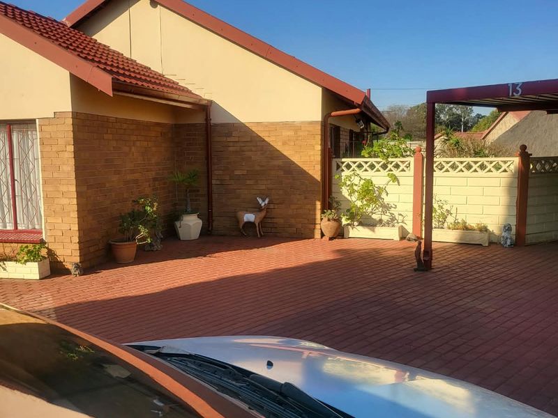 Front exterior view of the property featuring a brick facade, tiled roof, paved driveway, and a covered carport area.