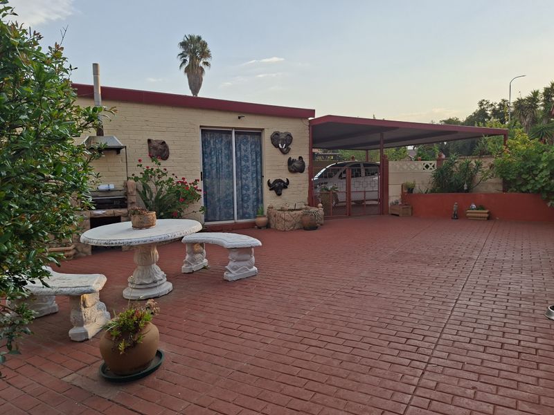A paved outdoor patio area featuring a built-in braai, covered carport, and direct access to the home via a sliding door.