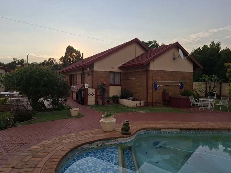 Rear view of the property featuring a brick facade, tiled roof, and a swimming pool with surrounding brick paving.