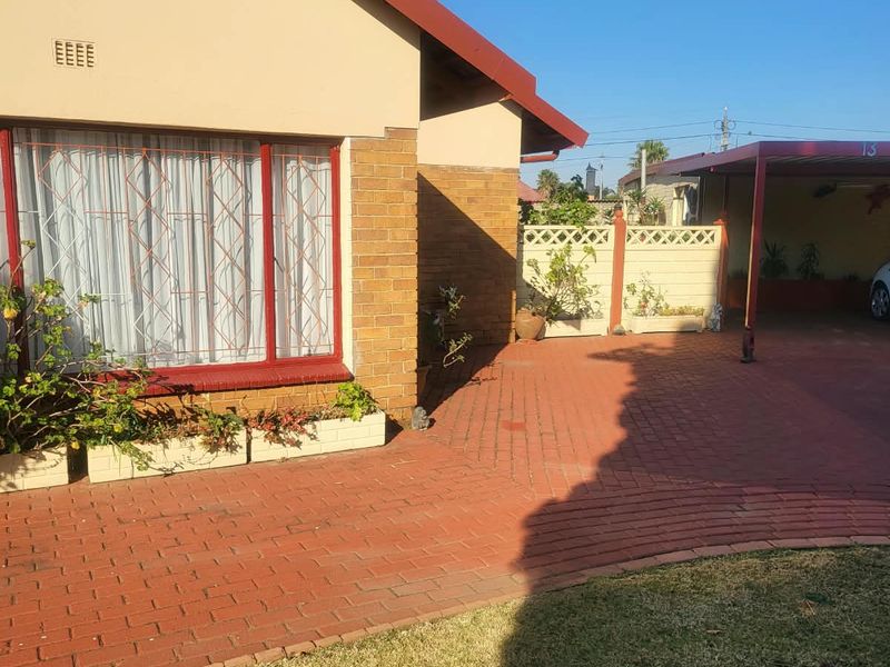 Front exterior view of the house featuring brick paving, a carport, and a secure boundary wall.
