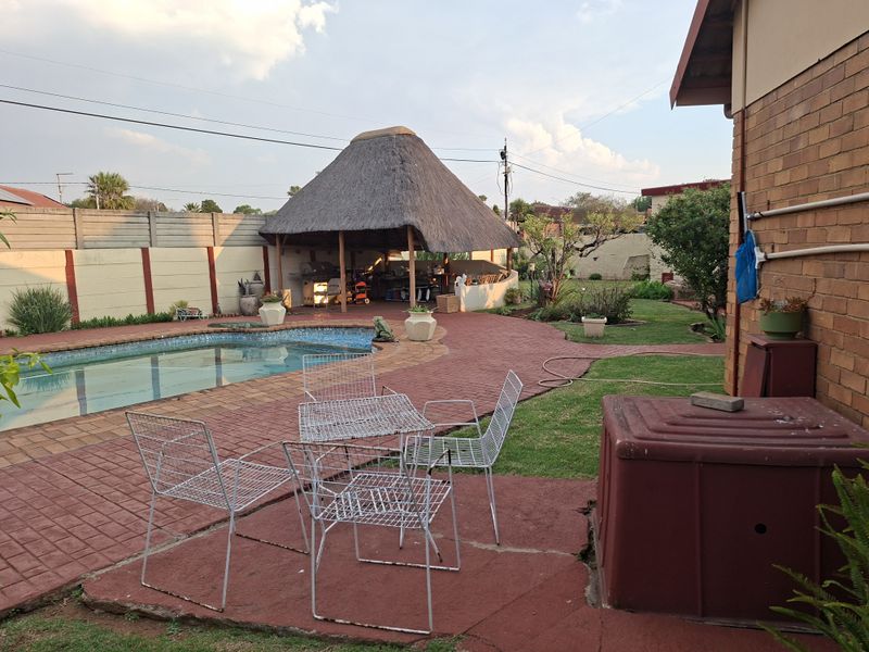 Outdoor entertainment area featuring a swimming pool, brick paving, and a traditional thatched lapa structure in a private garden setting.