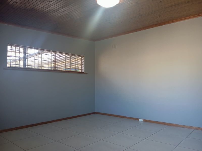 An empty living room featuring ceramic floor tiles, a timber tongue and groove ceiling, and horizontal venetian blinds.