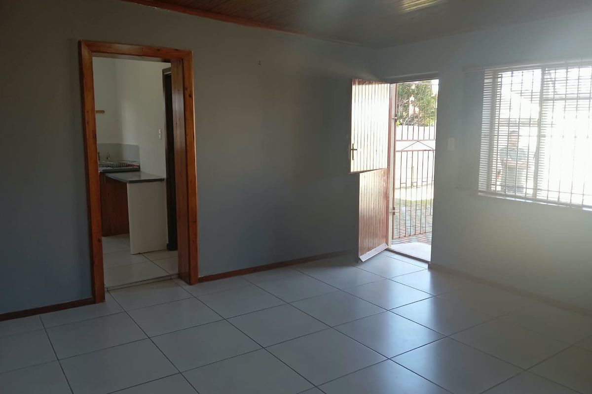 An empty living room featuring tiled flooring, timber ceiling, and direct access to the exterior through a security door.