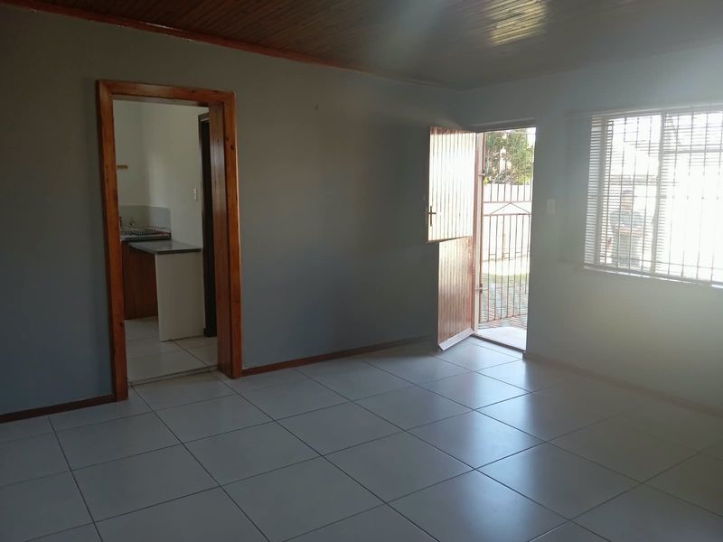 An empty living room featuring tiled flooring, timber ceiling, and direct access to the exterior through a security door.