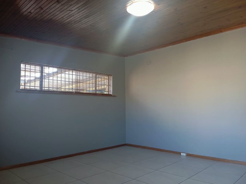 A spacious, empty bedroom featuring tiled flooring and a classic timber tongue and groove ceiling, providing a neutral canvas for personalization.