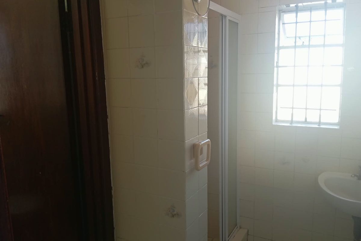 A dated bathroom featuring a shower enclosure, wall-mounted basin, and tiled walls with security bars on the window.