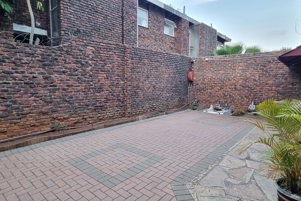 A private rear courtyard featuring paved flooring and high exposed brick boundary walls with security features.