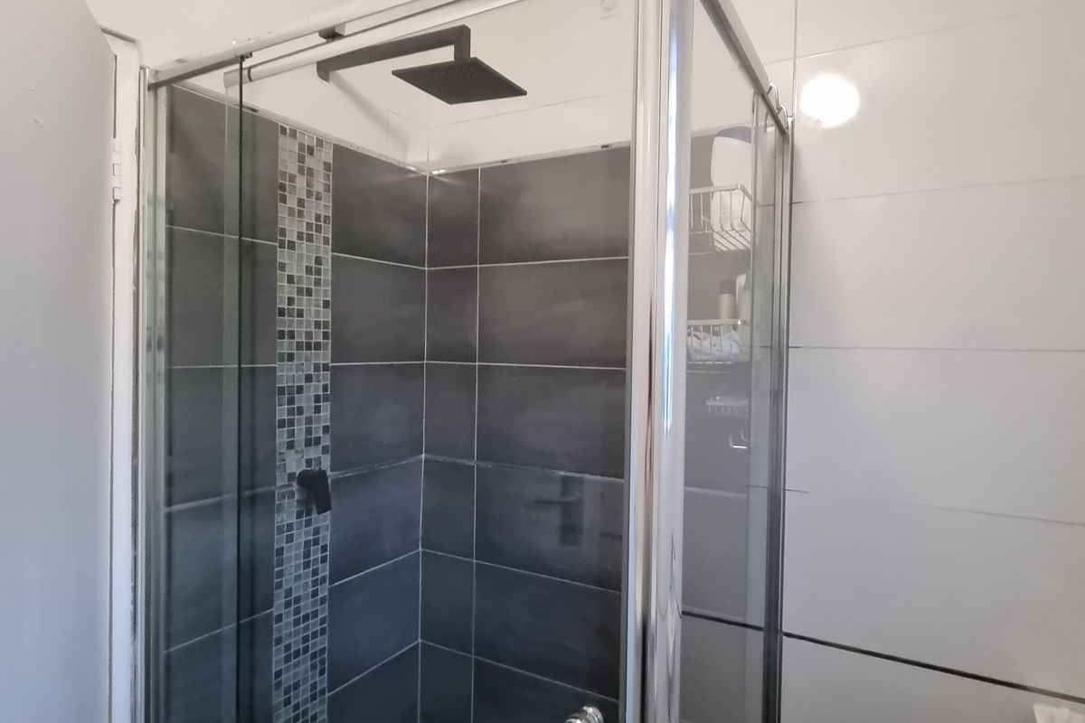 A bathroom featuring a corner shower enclosure with dark grey tiles, a mosaic accent strip, and a modern rain shower head.