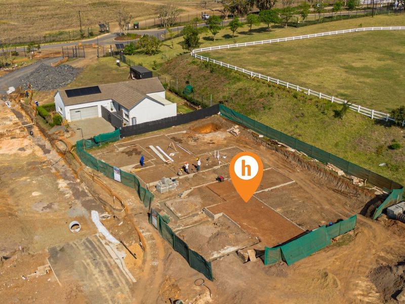 Aerial view of a residential construction site showing the concrete foundation slab and surrounding land development.
