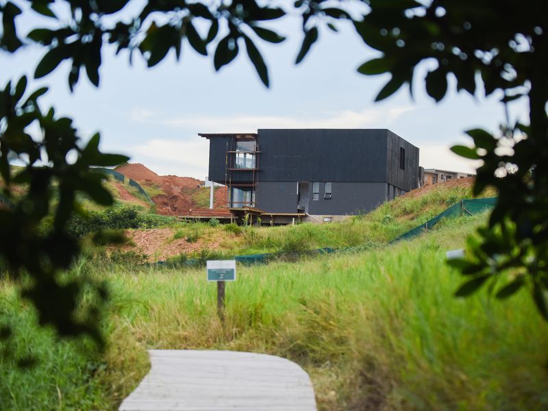 A view of a modern black-clad residential property under construction, featuring timber decking and surrounding undeveloped land.