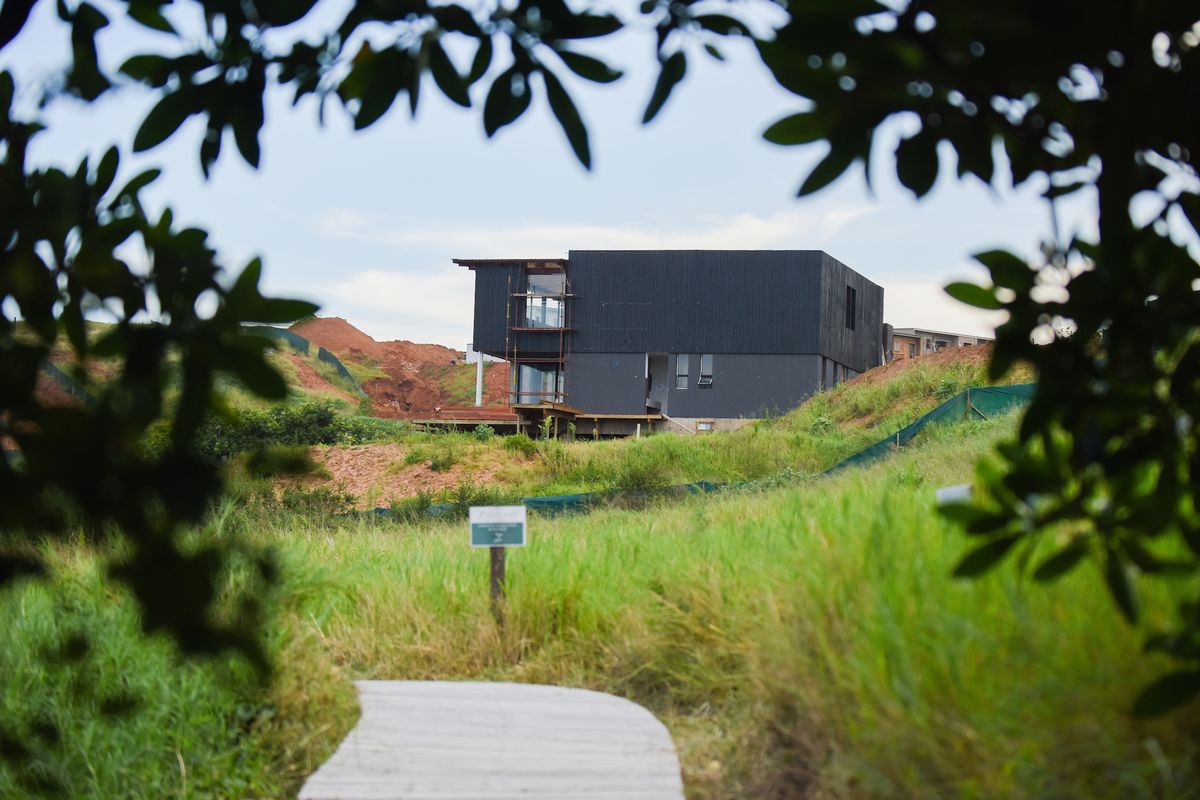 A view of a modern black-clad residential property under construction, featuring timber decking and surrounding undeveloped land.