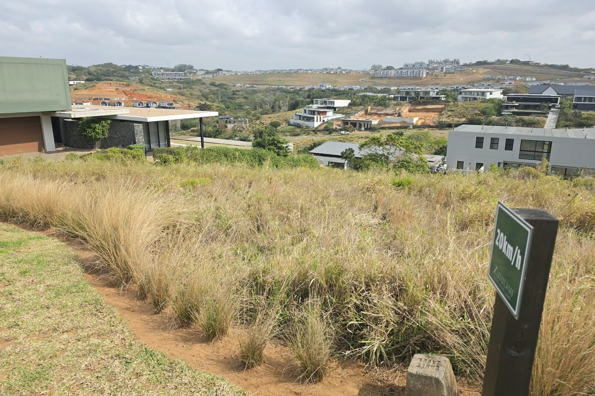 Elevated view overlooking a residential estate with sloped, undeveloped land in the foreground and surrounding modern architectural developments.