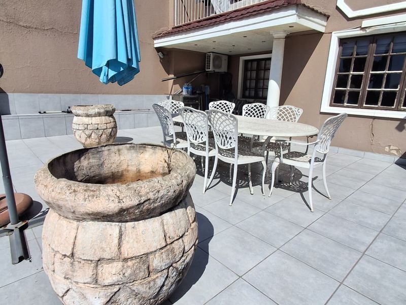 Spacious outdoor patio area featuring tiled flooring, a covered balcony section, and exterior wall lighting, suitable for outdoor dining and entertainment.