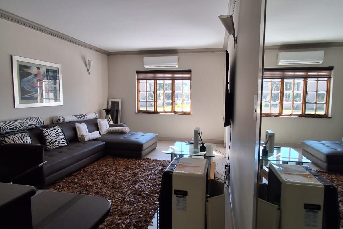 A well-maintained living room featuring tiled floors, crown molding, a split-system air conditioner, and a large wall mirror reflecting the space.