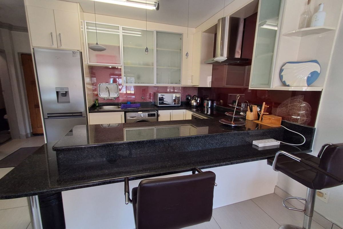 Modern kitchen featuring dark granite countertops, a glass splashback, stainless steel extractor fan, and ample built-in cabinetry with a breakfast bar.