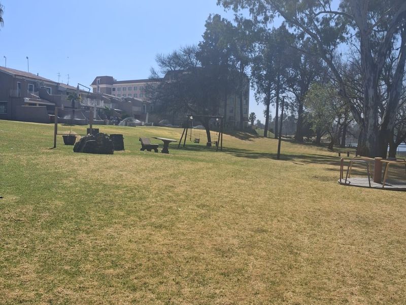 A spacious communal garden area featuring mature trees, expansive lawn, and playground equipment, providing an open outdoor space for residents.