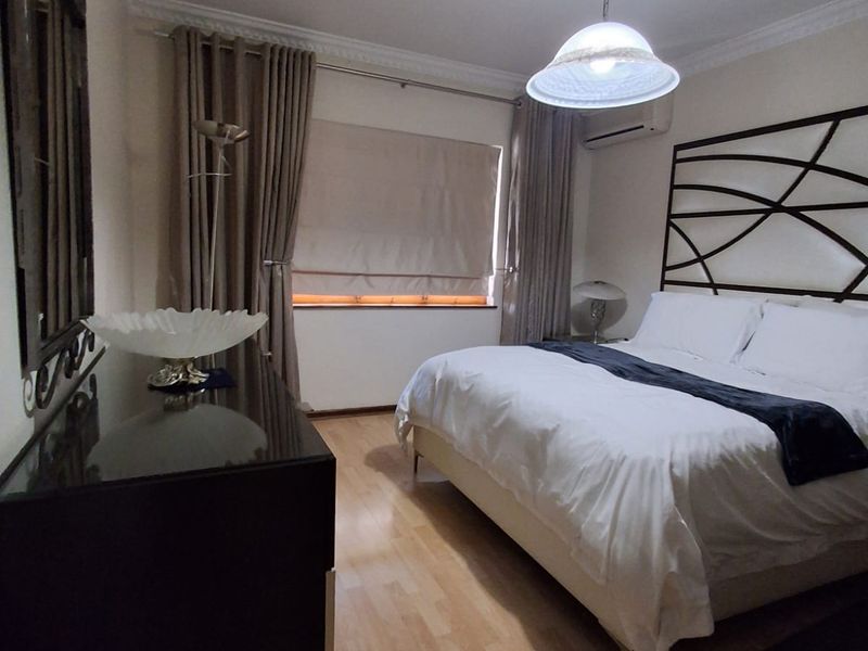 A well-maintained bedroom featuring laminate flooring, crown molding, and a wall-mounted air conditioning unit.
