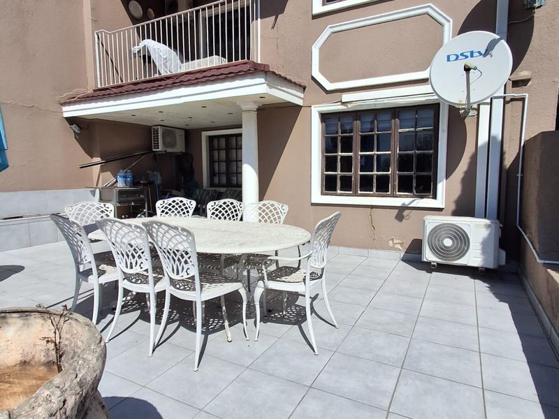A paved outdoor patio area featuring a covered balcony section, exterior wall mounted air conditioning units, and a satellite dish installation.