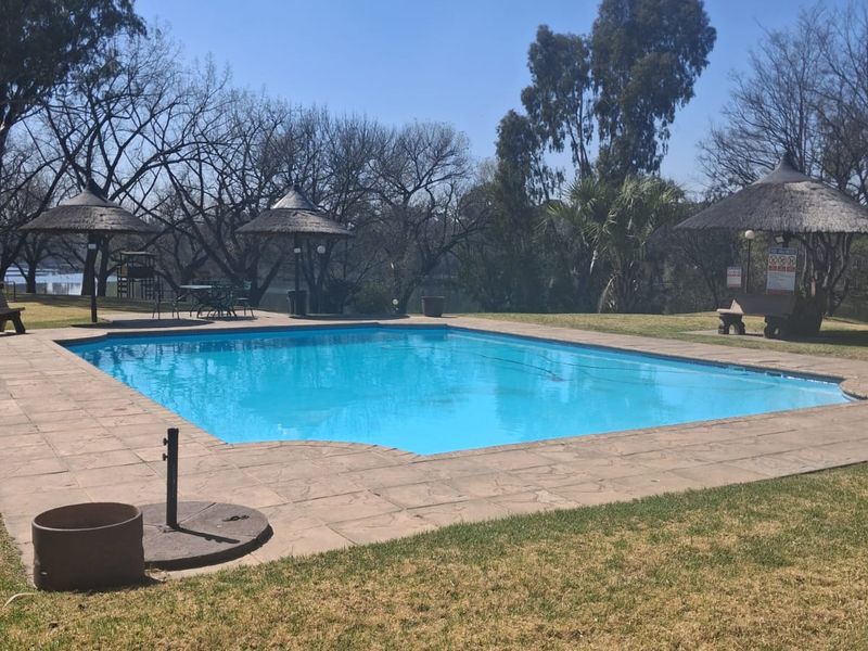Outdoor swimming pool area featuring a paved deck, thatch umbrellas, and surrounding lawn, providing a pleasant communal recreational space.