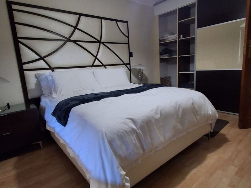 A well-maintained bedroom featuring laminate flooring, decorative ceiling cornicing, and a large built-in wardrobe with integrated shelving.
