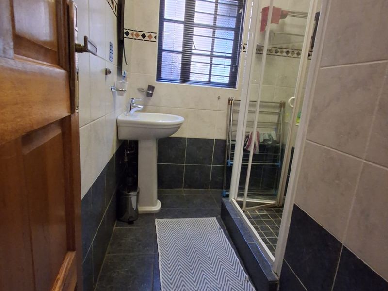 A functional bathroom featuring a pedestal basin, a glass-enclosed shower, and two-tone wall tiling with a decorative border.