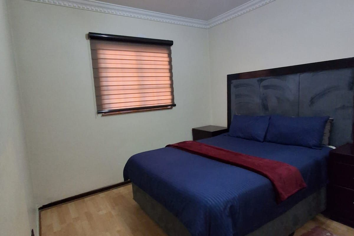 A well-maintained bedroom featuring laminate flooring, ceiling cornice detailing, an air conditioning unit, and modern roller blinds.