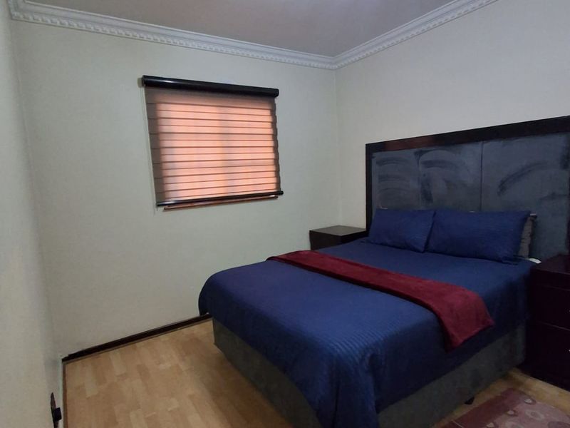 A well-maintained bedroom featuring laminate flooring, ceiling cornice detailing, an air conditioning unit, and modern roller blinds.