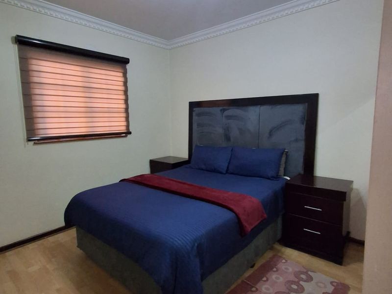 A well-maintained bedroom featuring laminate flooring, crown molding, and a fitted roller blind, providing a clean and functional living space.