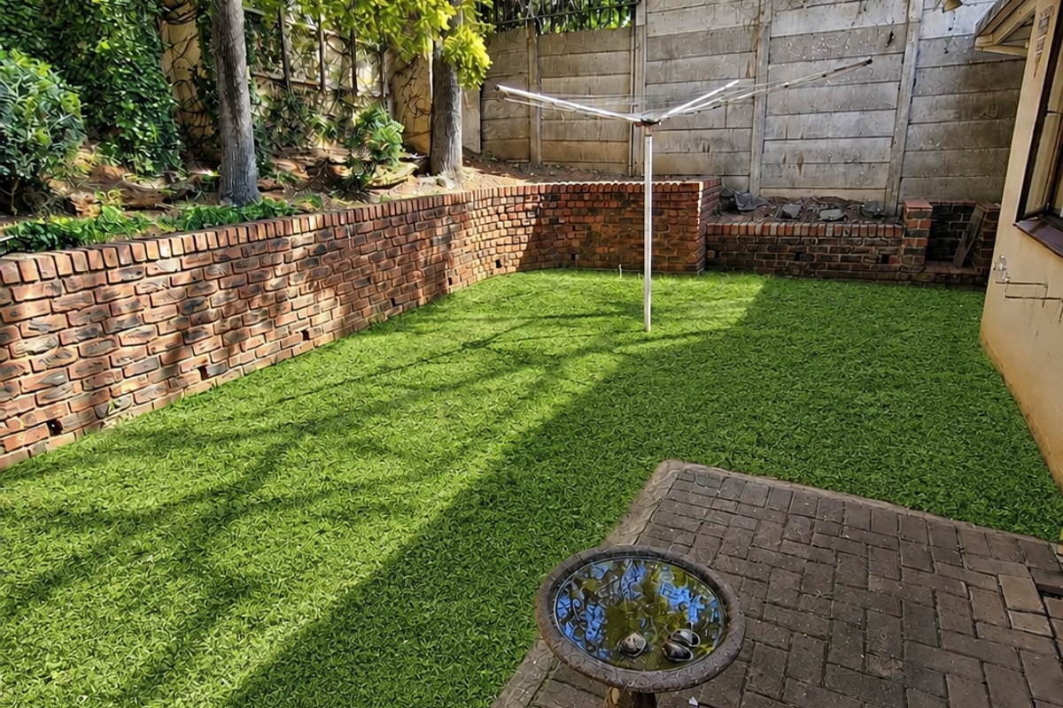 A private rear garden featuring a paved patio area, artificial lawn, brick retaining walls, and secure perimeter fencing.